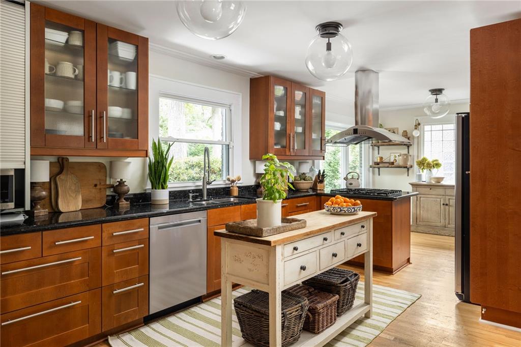 Kitchen with warm wood cabinets, black counters, and a cream-colored island beneath a stainless range hood.