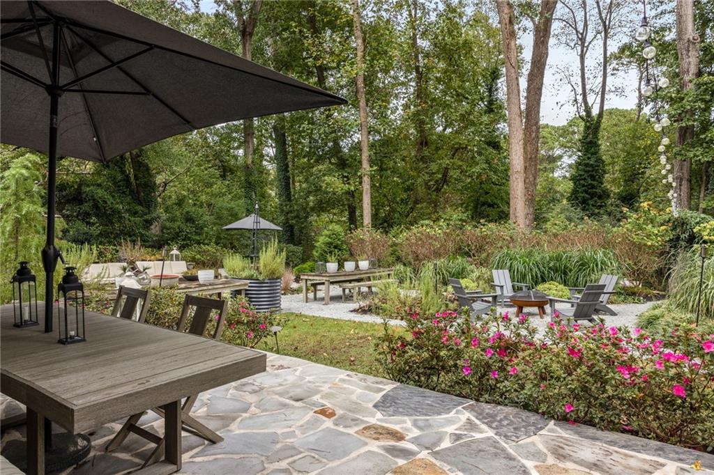 Landscaped backyard patio with a stone terrace, umbrella-covered dining table, and gravel seating area.