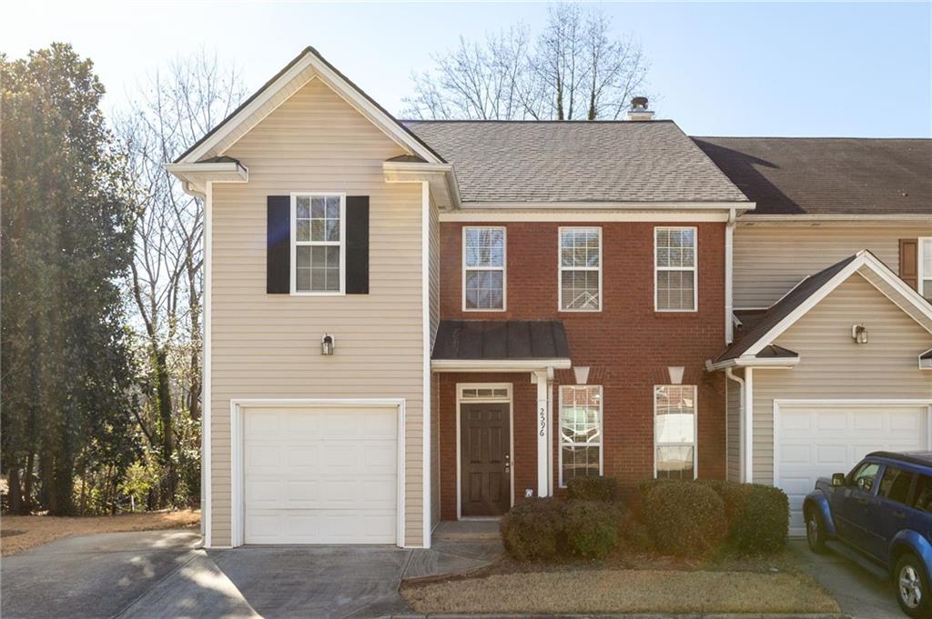 Two-story townhouse with beige siding, a red brick center, and two garage doors.