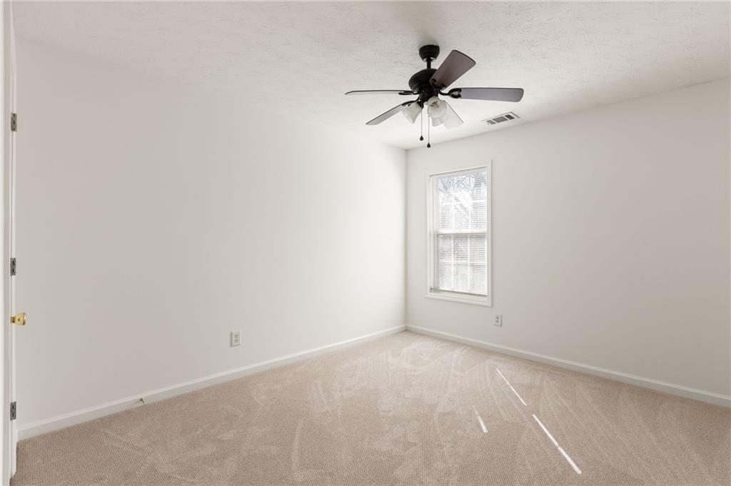 Empty carpeted bedroom with a ceiling fan and a window with blinds.