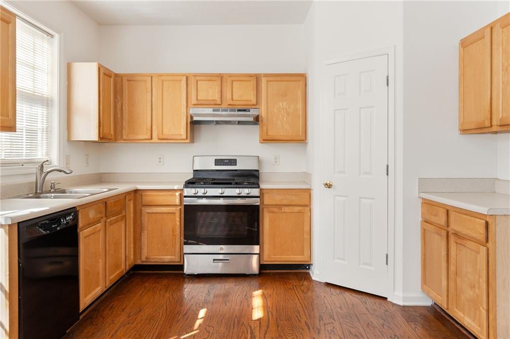 Kitchen with honey-colored wood cabinets, stainless steel range, window-side sink, and dark hardwood floors.