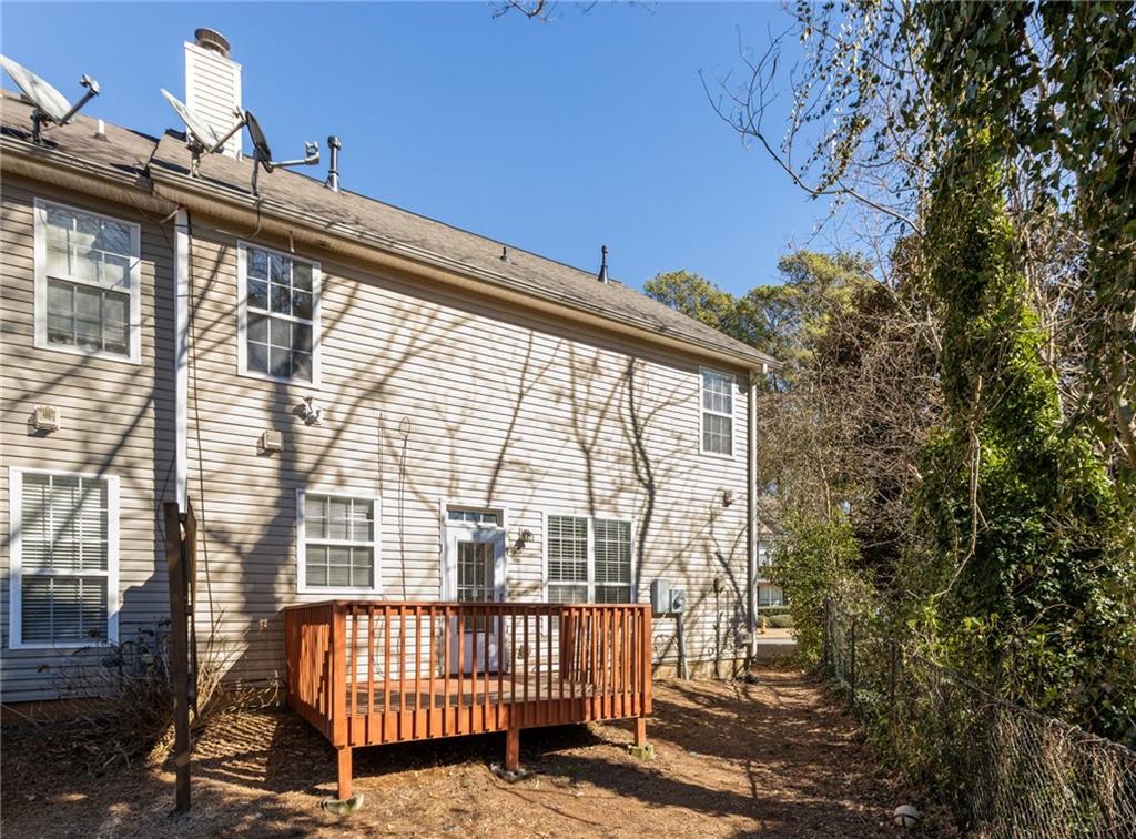 Rear of a two-story beige house with a small raised deck and a tree-lined fenced yard.