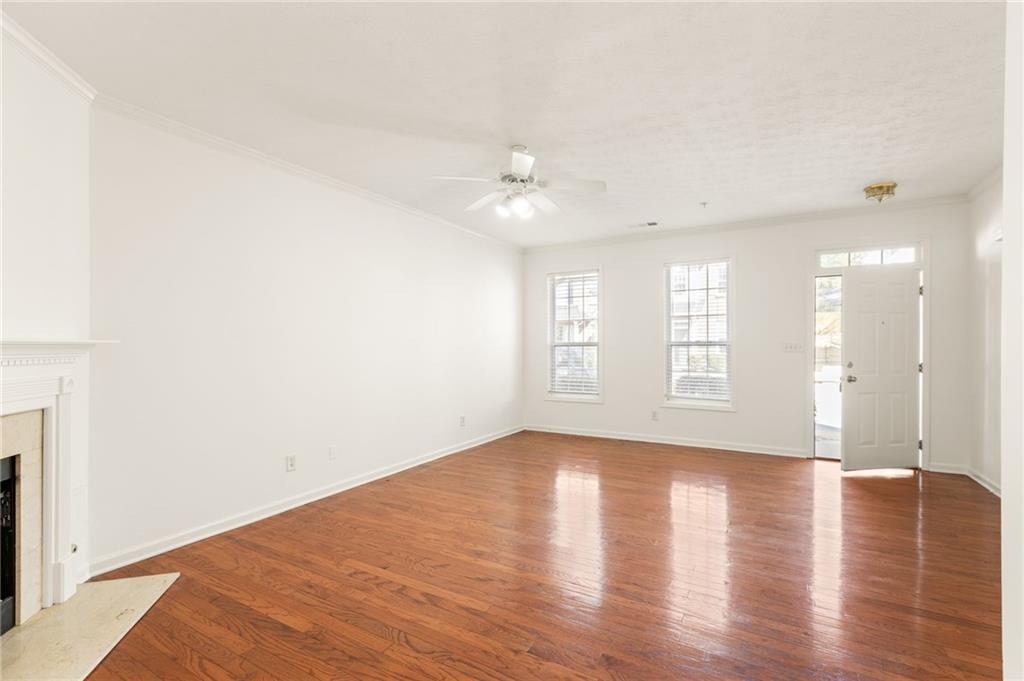 Empty living room with hardwood floors, a fireplace, ceiling fan, and open front door.