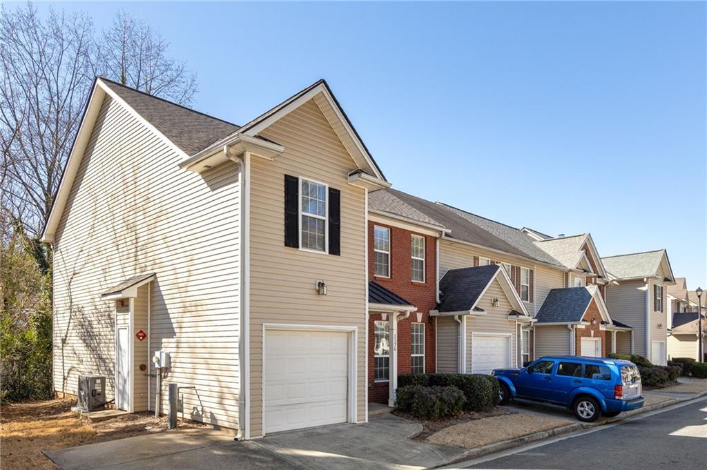 Attached townhouse with beige siding, red-brick facade, white garage door, and a blue SUV in the driveway.