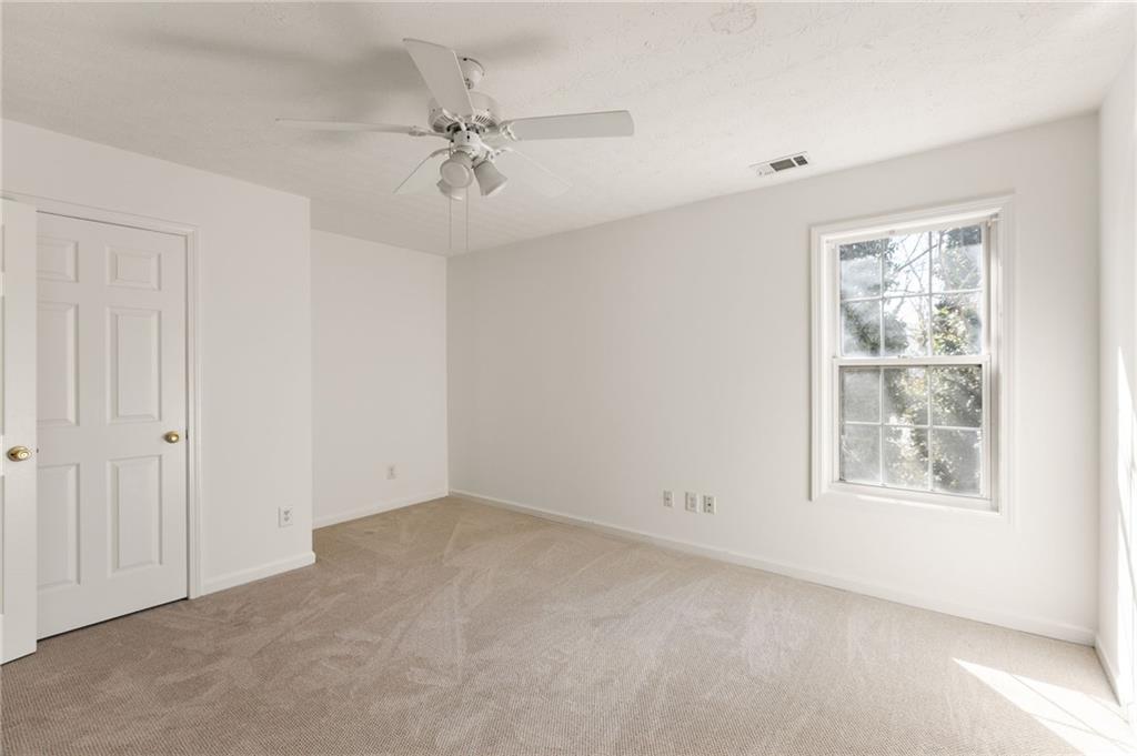 Empty bedroom with beige carpet, a ceiling fan, and a sunlit window.