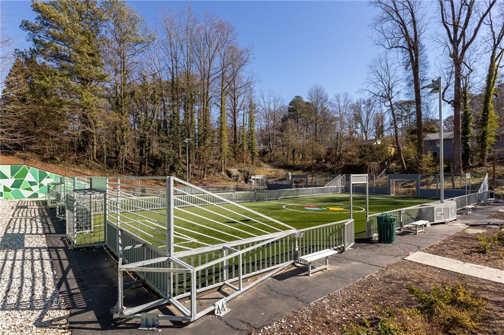 Fenced artificial-turf sports court with white markings, benches, and leafless trees.