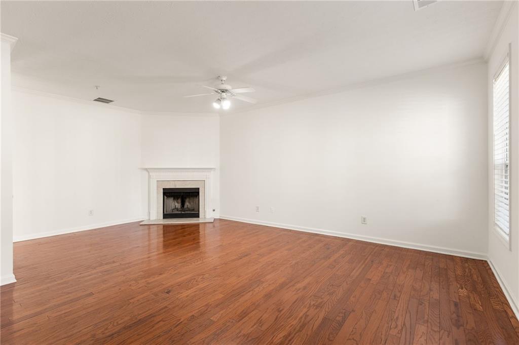 Empty living room with hardwood floors, a white fireplace, and ceiling fan.