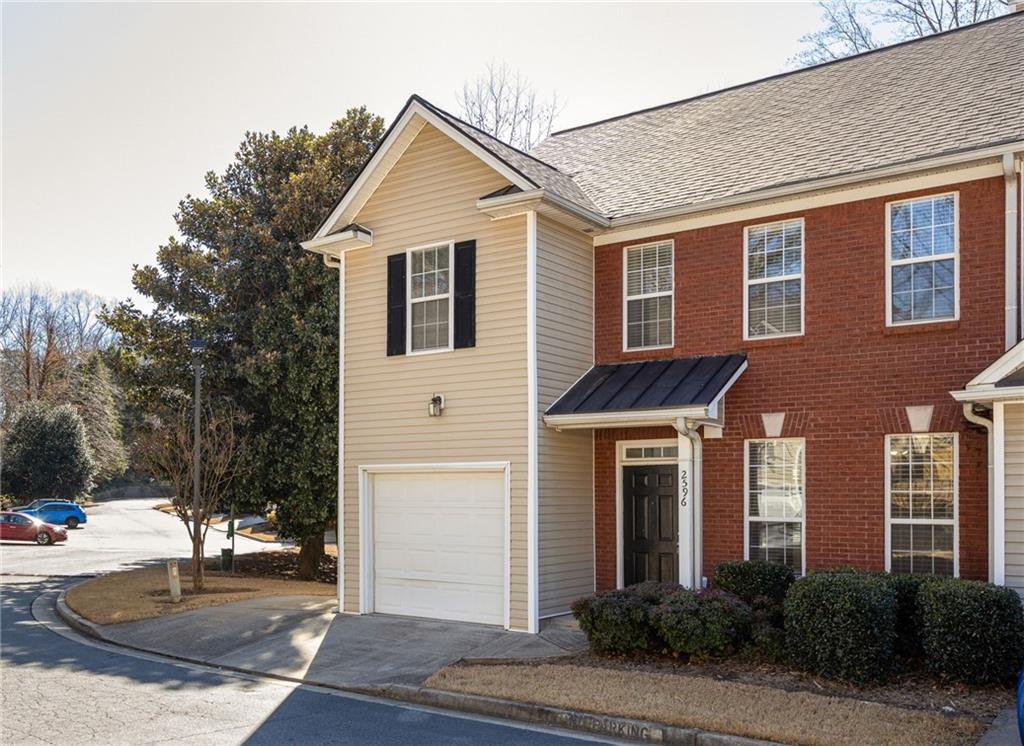 Two-story attached home with red brick, beige siding, a single garage, and black entry awning.