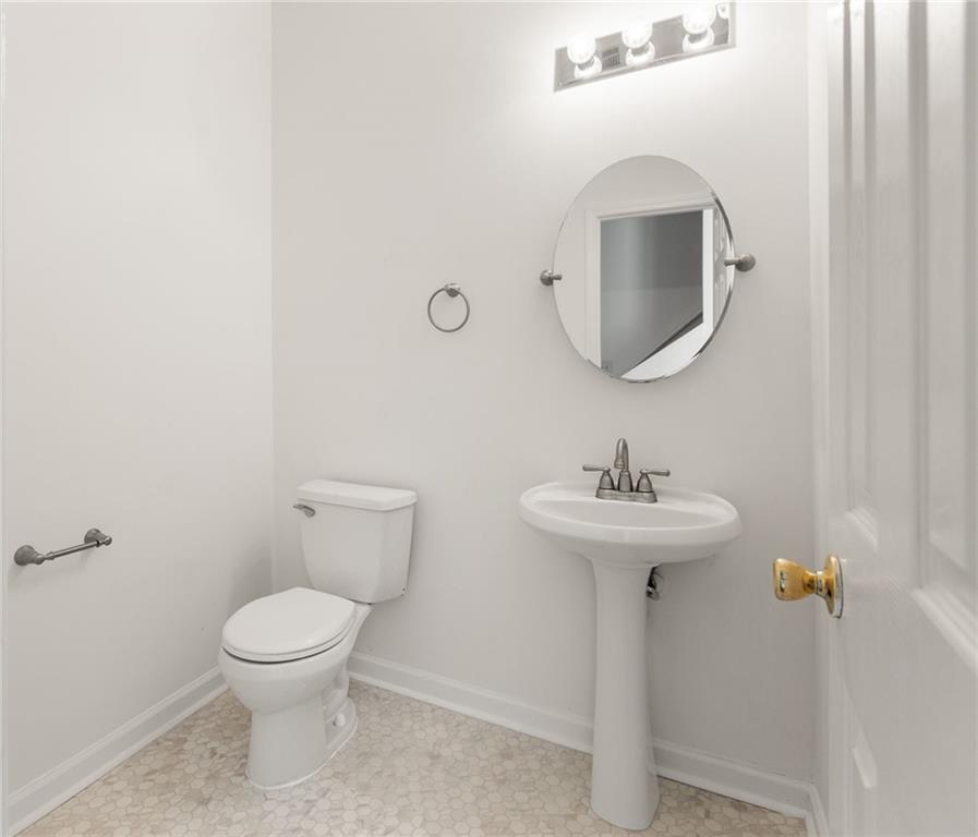 Powder room with a pedestal sink, round mirror, and pale hexagonal tile floor.