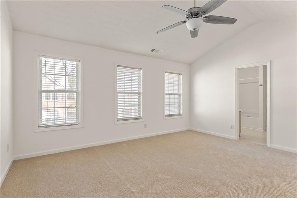 Empty bedroom with beige carpet, three shuttered windows, and a ceiling fan.