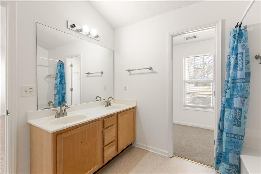 Bathroom with a double-sink wood vanity, large mirror, and blue patterned shower curtain.