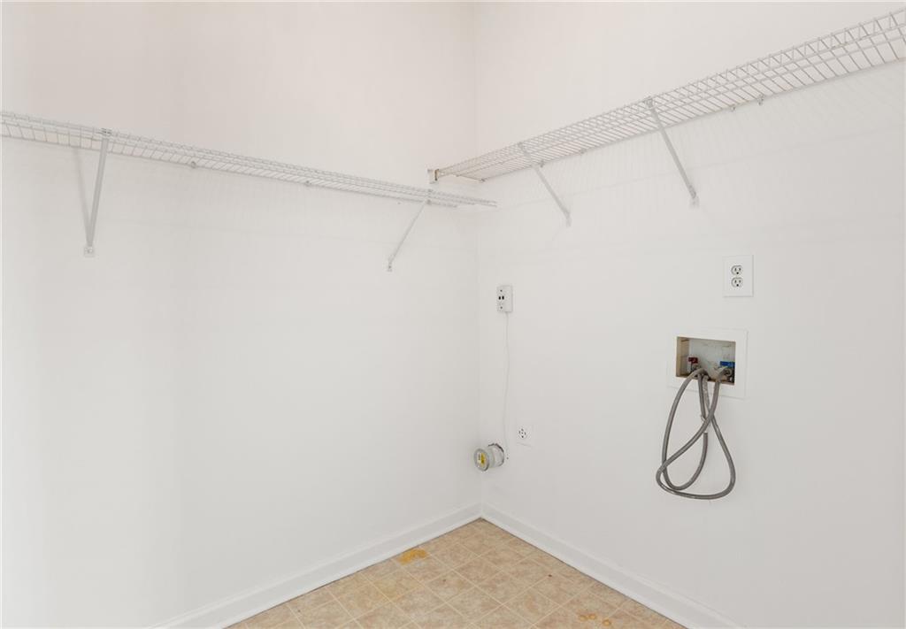 Empty laundry room with wire shelving, washer and dryer hookups, and beige patterned flooring.