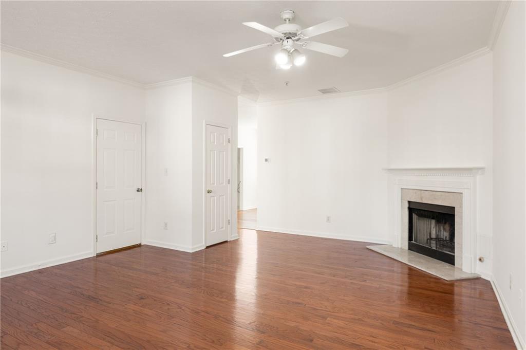 Empty living room with hardwood floors, a white ceiling fan, and a fireplace with a white mantel.