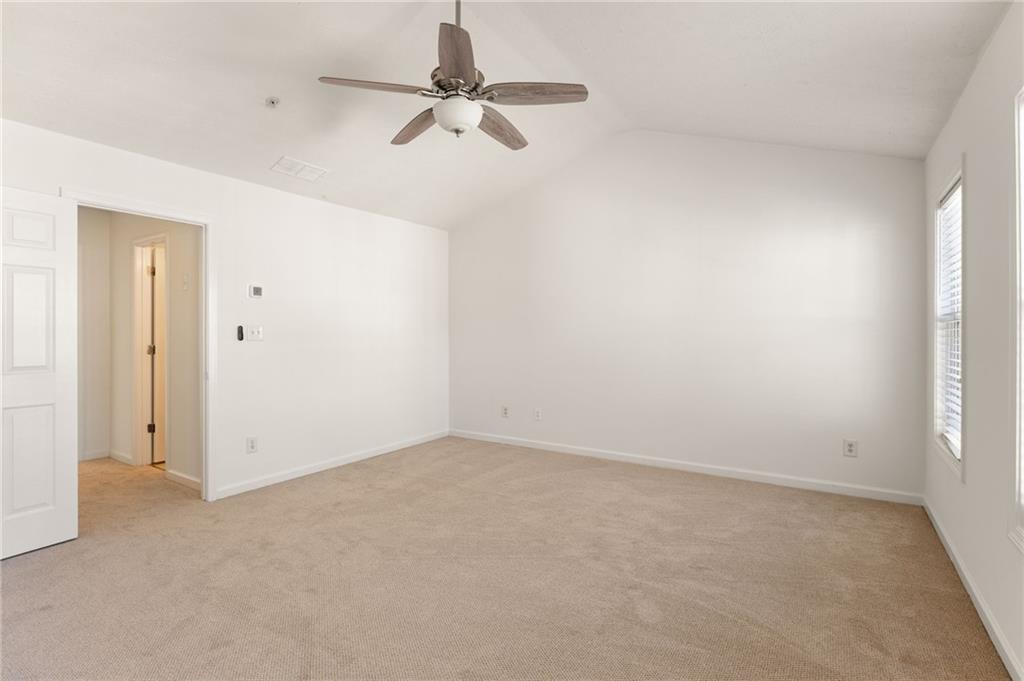 Empty bedroom with beige carpet, ceiling fan, and vaulted ceiling.