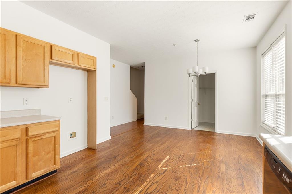 Empty kitchen and dining area with wood cabinets, hardwood floors, and a chandelier.