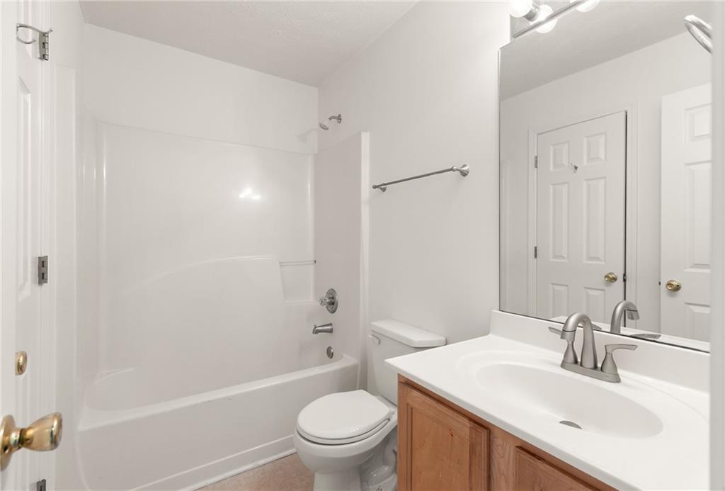 Bathroom with a white tub and shower, toilet, and wood vanity.