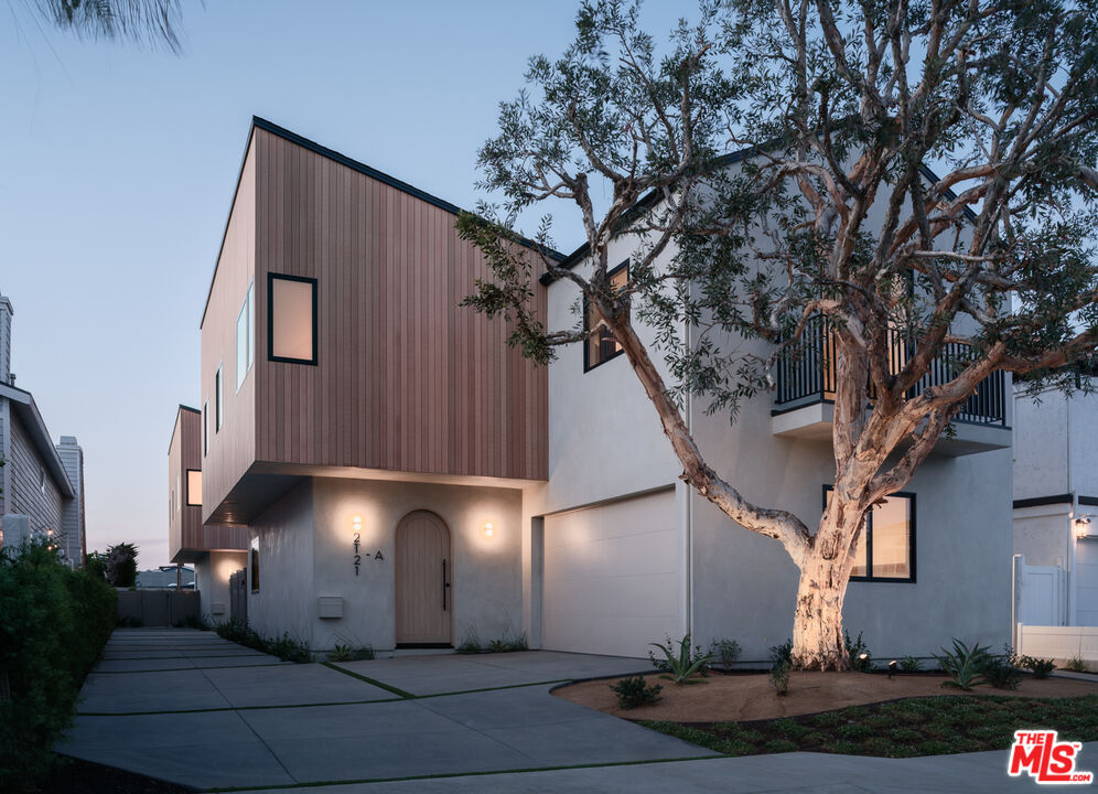 Modern two-story home with brown siding, an arched entry, and a large tree at dusk.