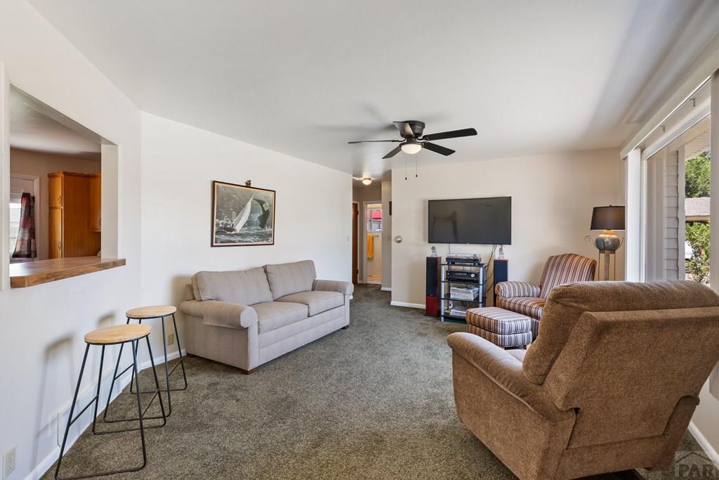 Furnished living room with gray carpet, a light sofa, recliners, and large windows.