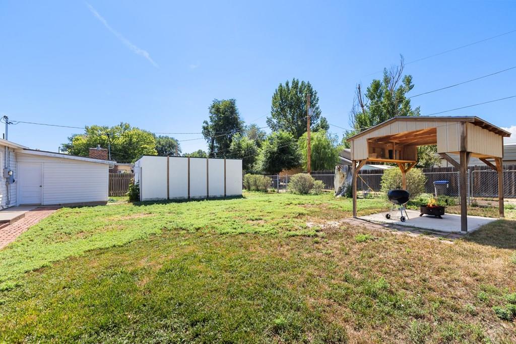 Backyard with a covered wooden pavilion and grill, lawn, and white storage shed.