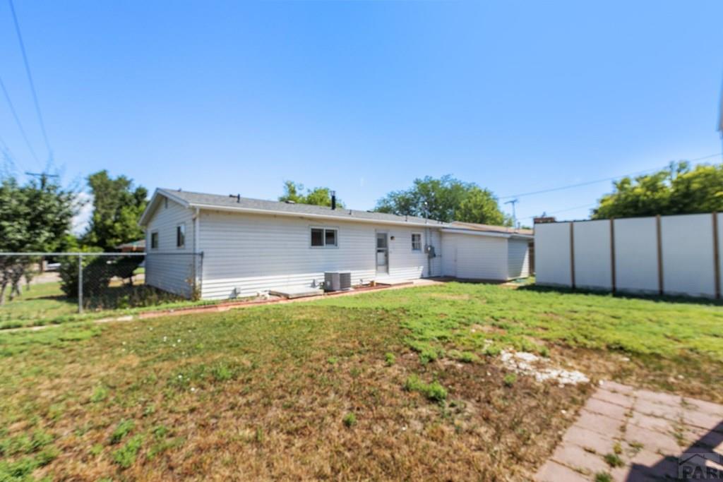 Single-story white house viewed from the backyard, with a patchy lawn and tall privacy fence.