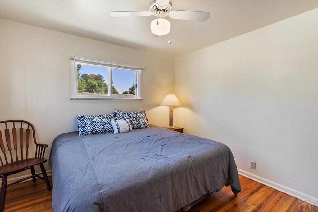Bedroom with a gray-covered bed, patterned pillows, a wooden chair, and hardwood floors.