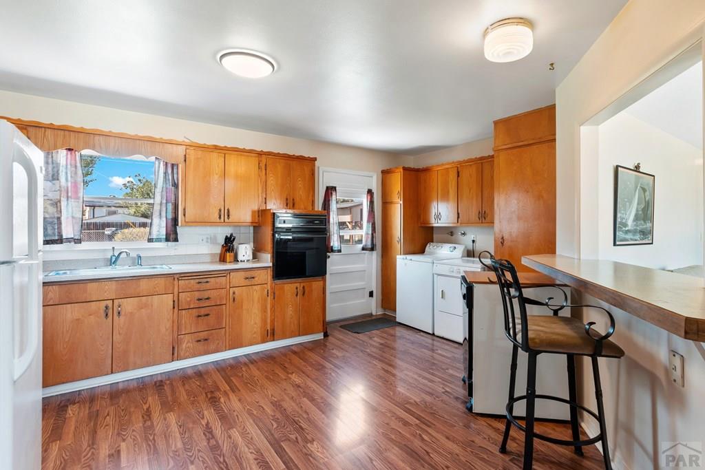 Kitchen with warm wood cabinets, laundry appliances by the back door, and a raised counter with bar stools.