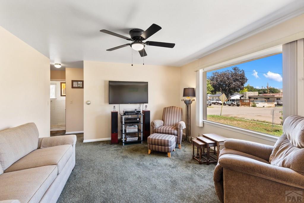 Furnished living room with beige sofas, striped armchairs, and a large street-facing window.
