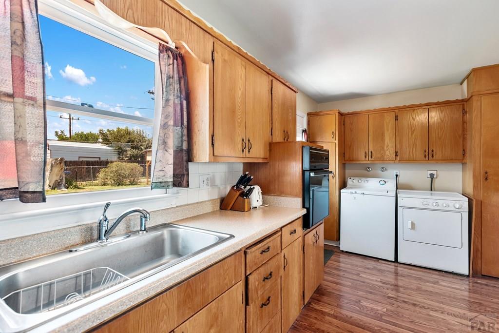 Kitchen with honey-colored cabinets, a double sink beneath a window, and a white washer and dryer.