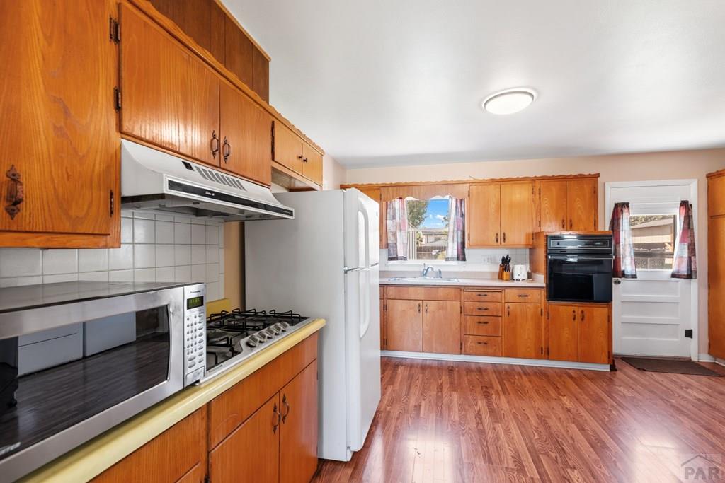 Kitchen with warm wood cabinets, a gas cooktop, white refrigerator, and wood-look flooring.