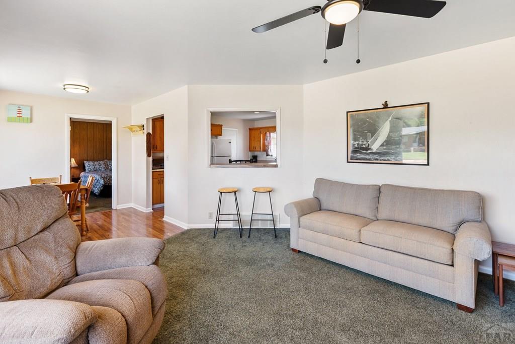 Living room with two sofas, gray carpet, and a pass-through window to the kitchen.