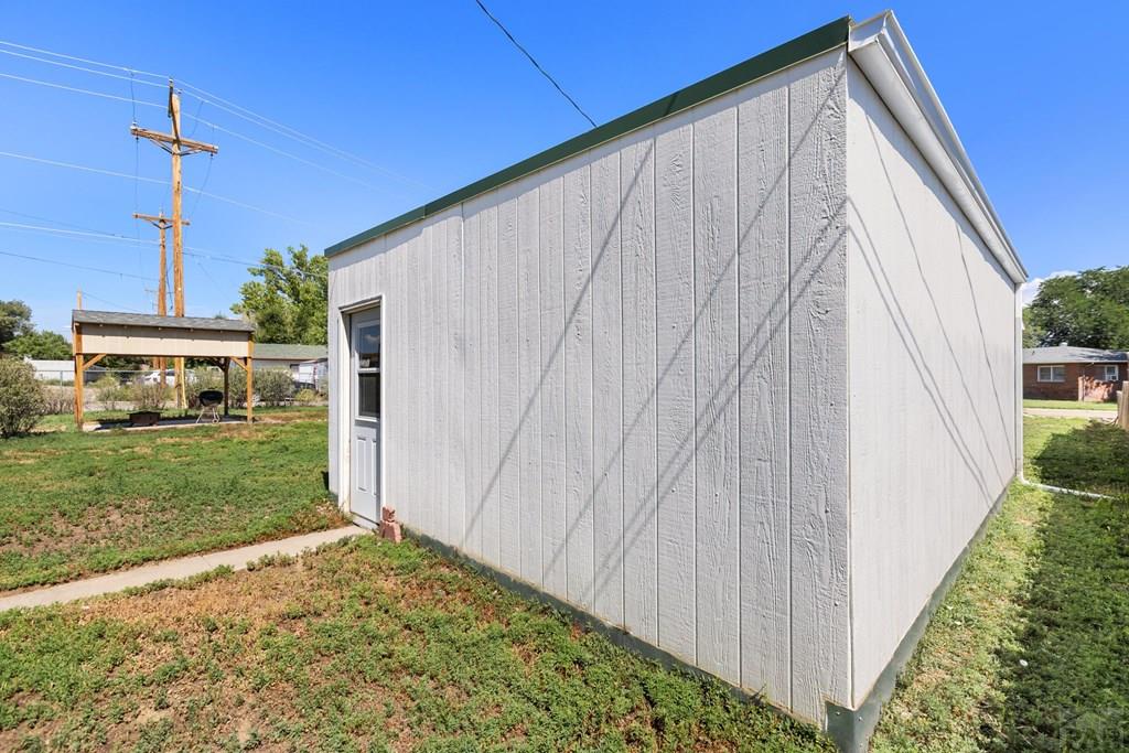 White detached outbuilding with vertical siding and a small side door in a grassy yard.