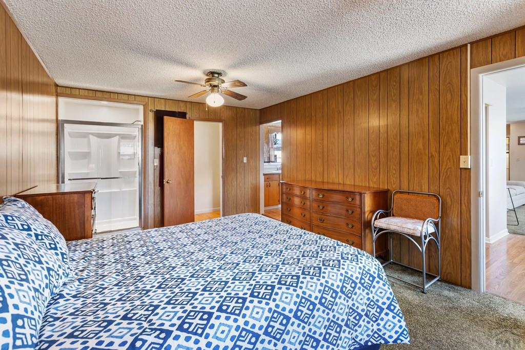 Bedroom with blue-and-white patterned bedding, wood-paneled walls, and a ceiling fan.