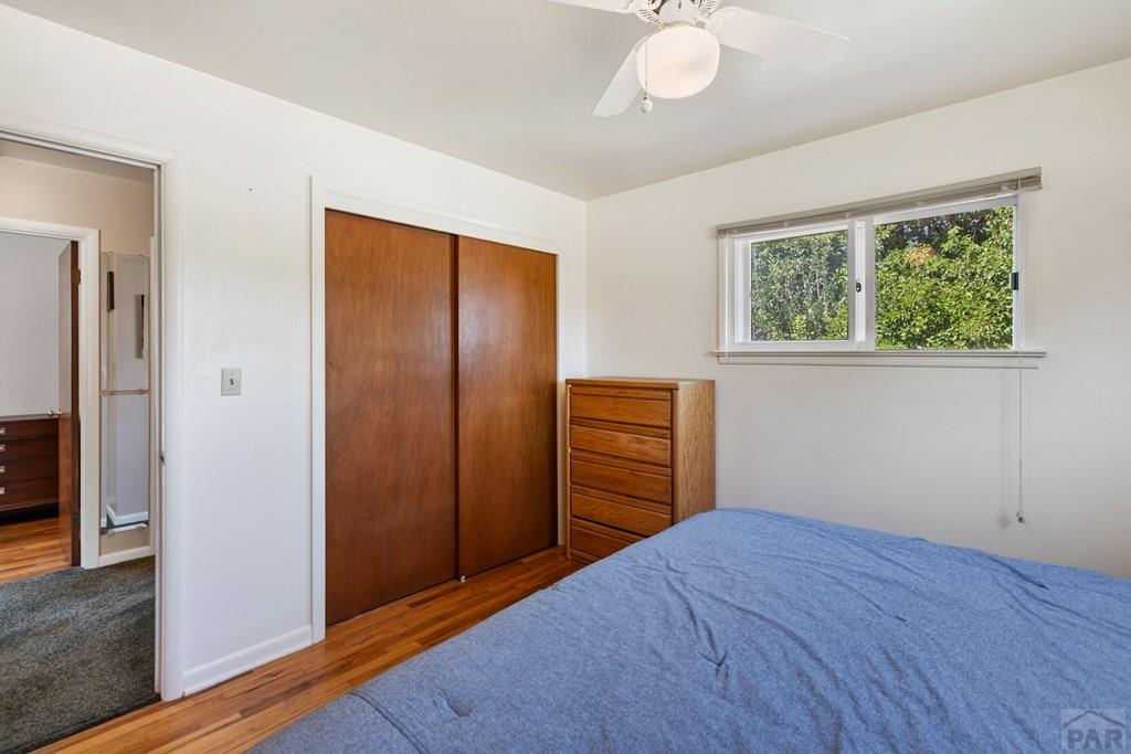 Bedroom with a blue bedspread, wood closet doors, and a window overlooking trees.