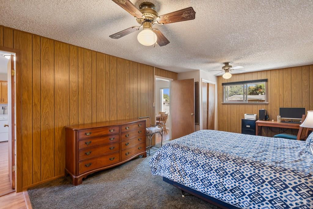 Bedroom with wood-paneled walls, patterned bedspread, wooden dresser, and two ceiling fans.