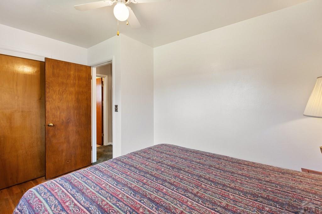 Bedroom with patterned bedspread, wooden sliding closet doors, and ceiling fan.