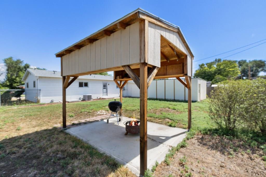 Backyard wooden patio shelter with a barbecue grill and fire pit on a concrete slab.