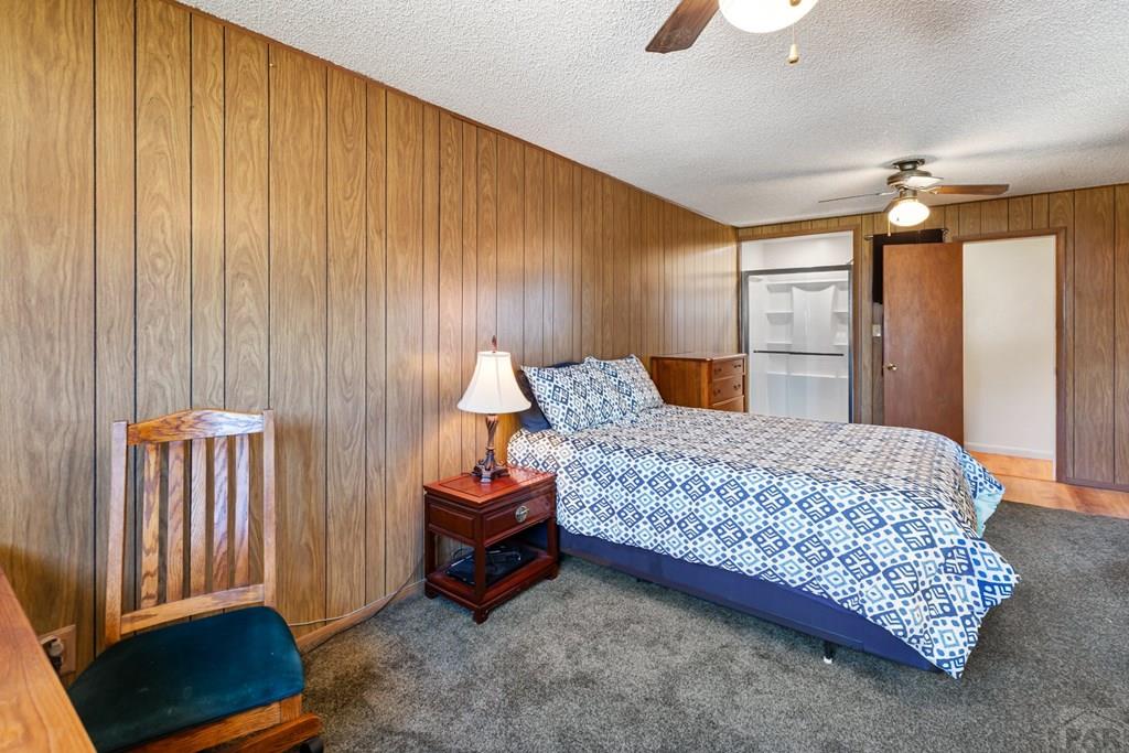 Bedroom with wood-paneled walls, patterned bedding, gray carpet, and a wooden chair.