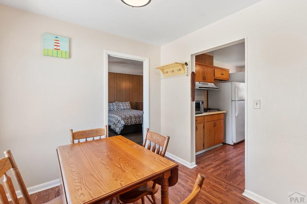 Dining room with a wooden table and chairs, wood flooring, and doorways to the kitchen and bedroom.