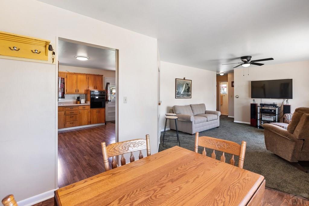 Dining area with a wooden table opens onto a carpeted living room and wood-cabinet kitchen.
