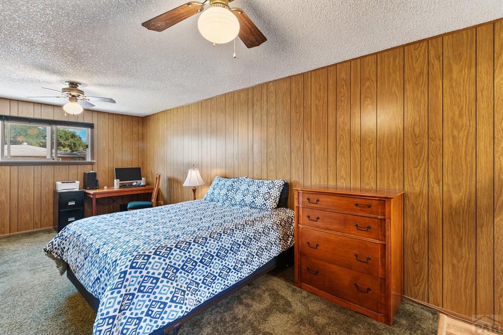 Bedroom with wood-paneled walls, blue-and-white patterned bedding, and a wooden dresser.