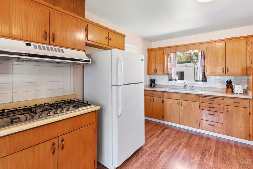 Kitchen with honey-colored wood cabinets, a white refrigerator, and a gas range.