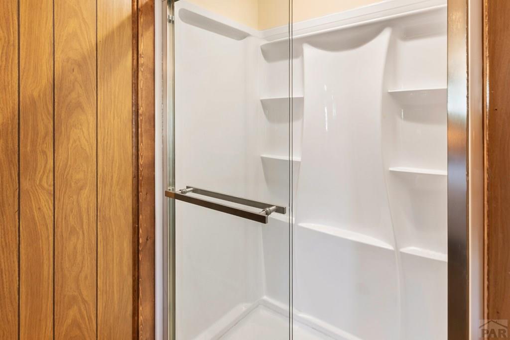White shower with built-in shelves and a clear glass door, framed by warm wood paneling.