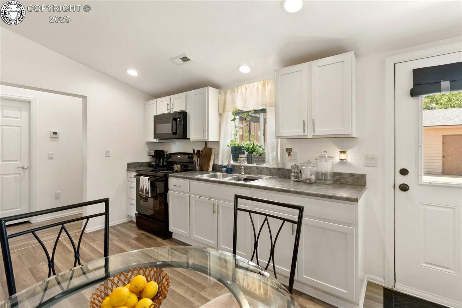 Kitchen with white cabinets, gray countertops, stainless appliances, and a glass dining table.