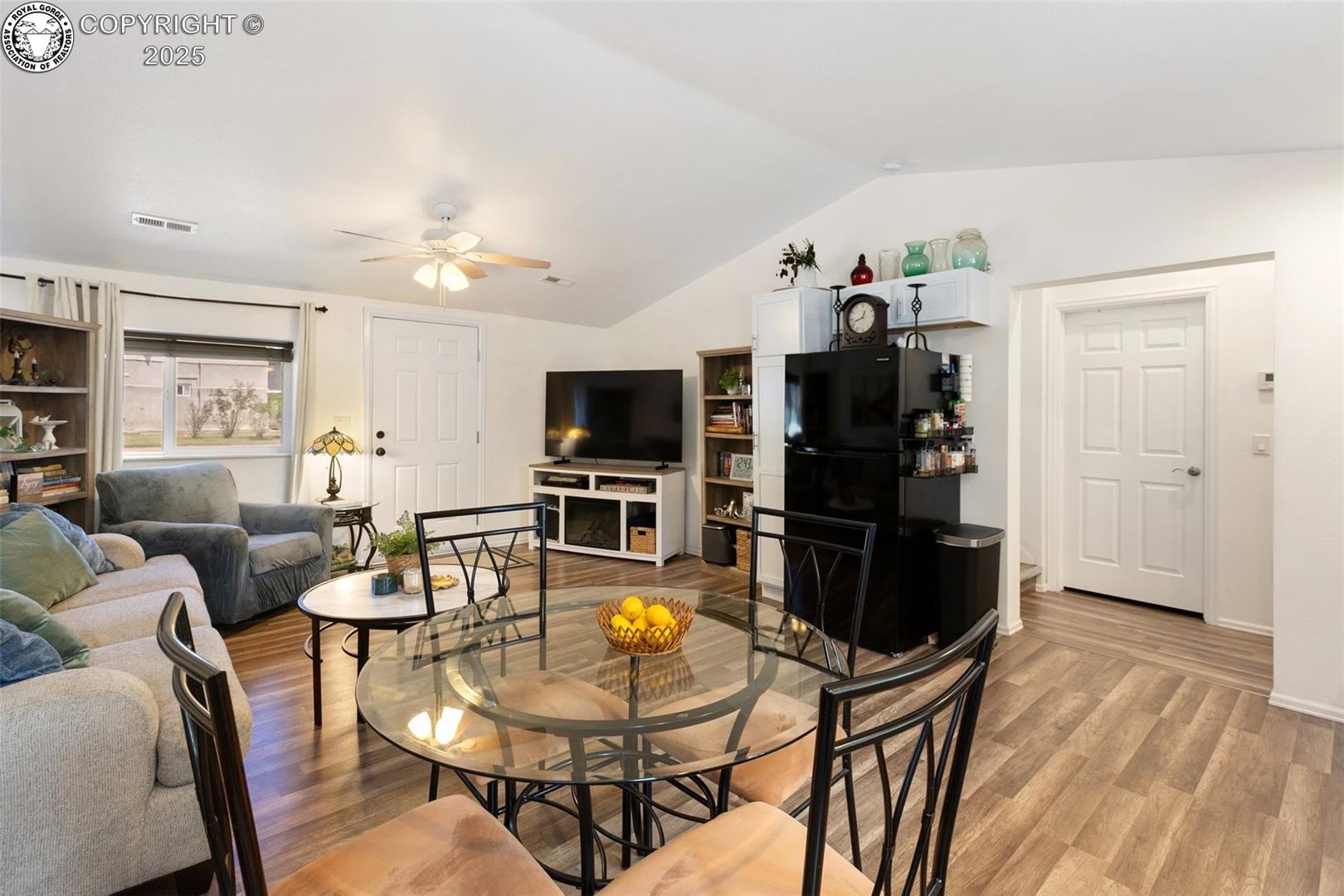 Furnished living and dining area with a glass table, sofas, television, and wood-look flooring.