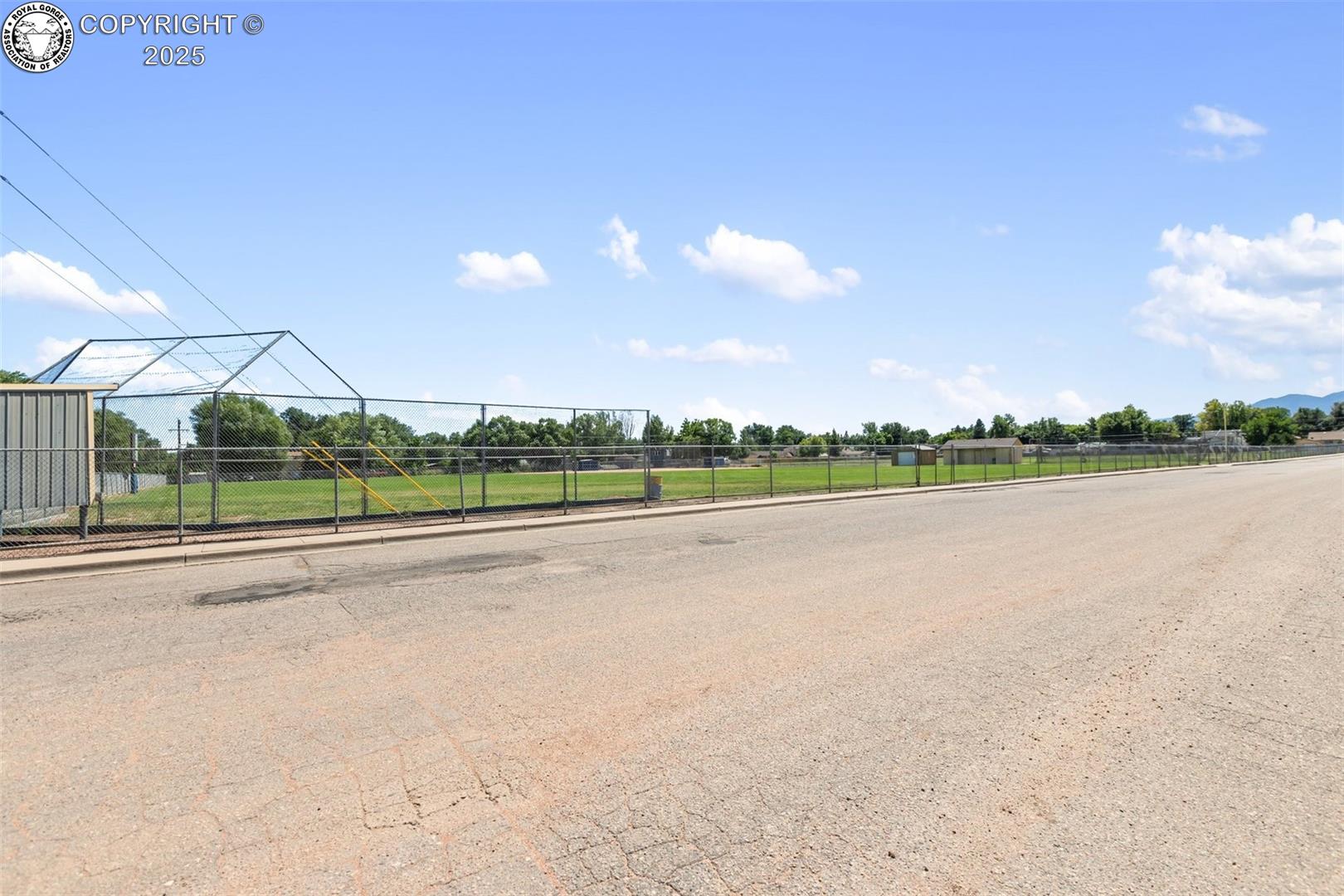 Fenced grassy lot beside a paved street, with a small metal-roofed structure.