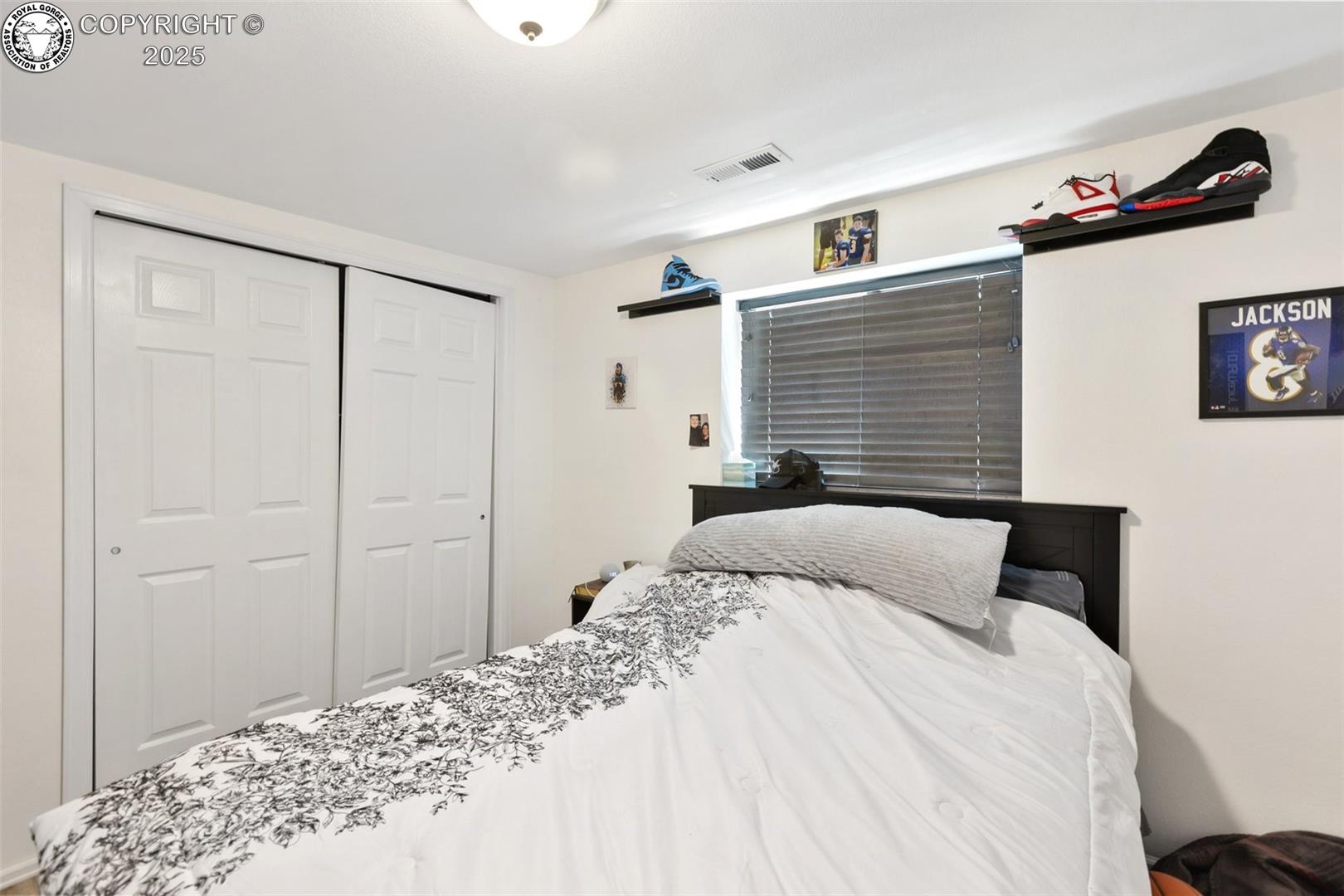 Bedroom with patterned white bedding, dark headboard, closed blinds, and sliding closet doors.