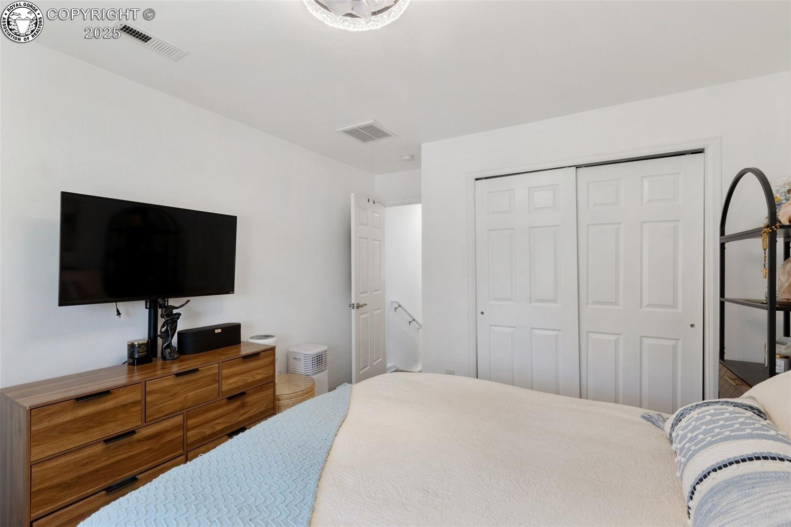 Bedroom with a white bed, blue quilt, wooden dresser, wall-mounted television, and sliding closet doors.