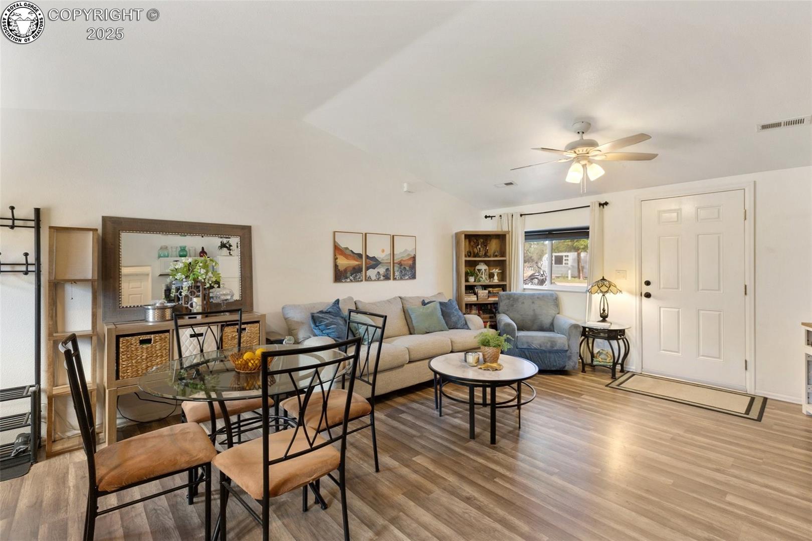 Furnished living and dining room with vaulted ceiling, gray seating, and wood-look flooring.
