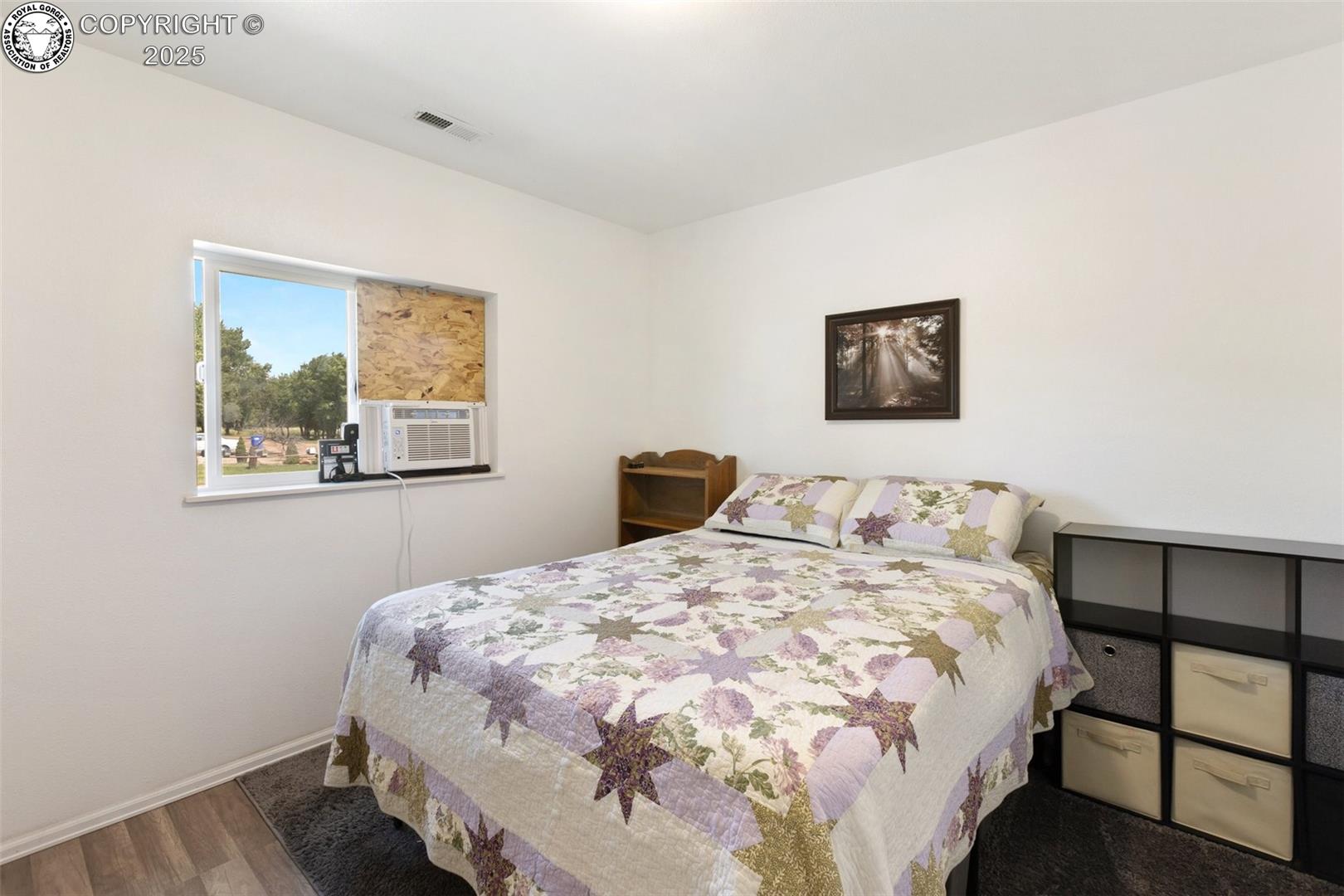 Bedroom with a floral quilted bed, window air conditioner, and cube storage.