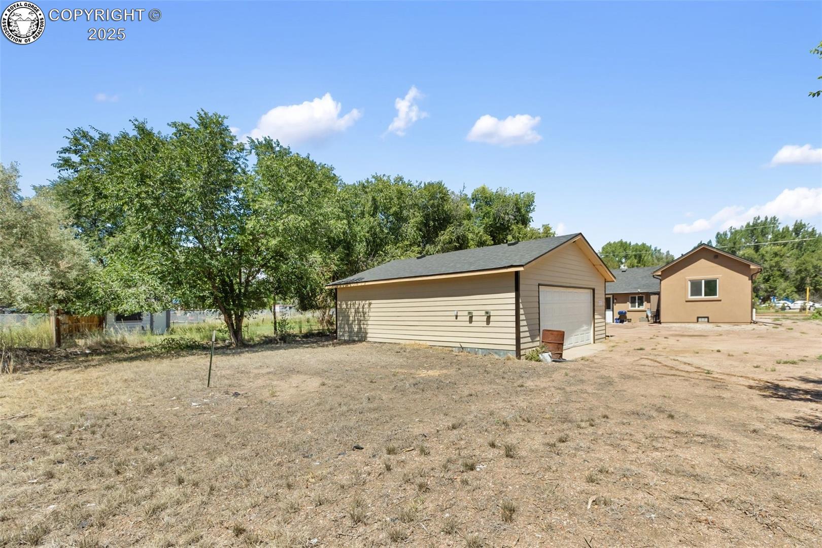 Detached garage and single-story home across a dry, open yard.